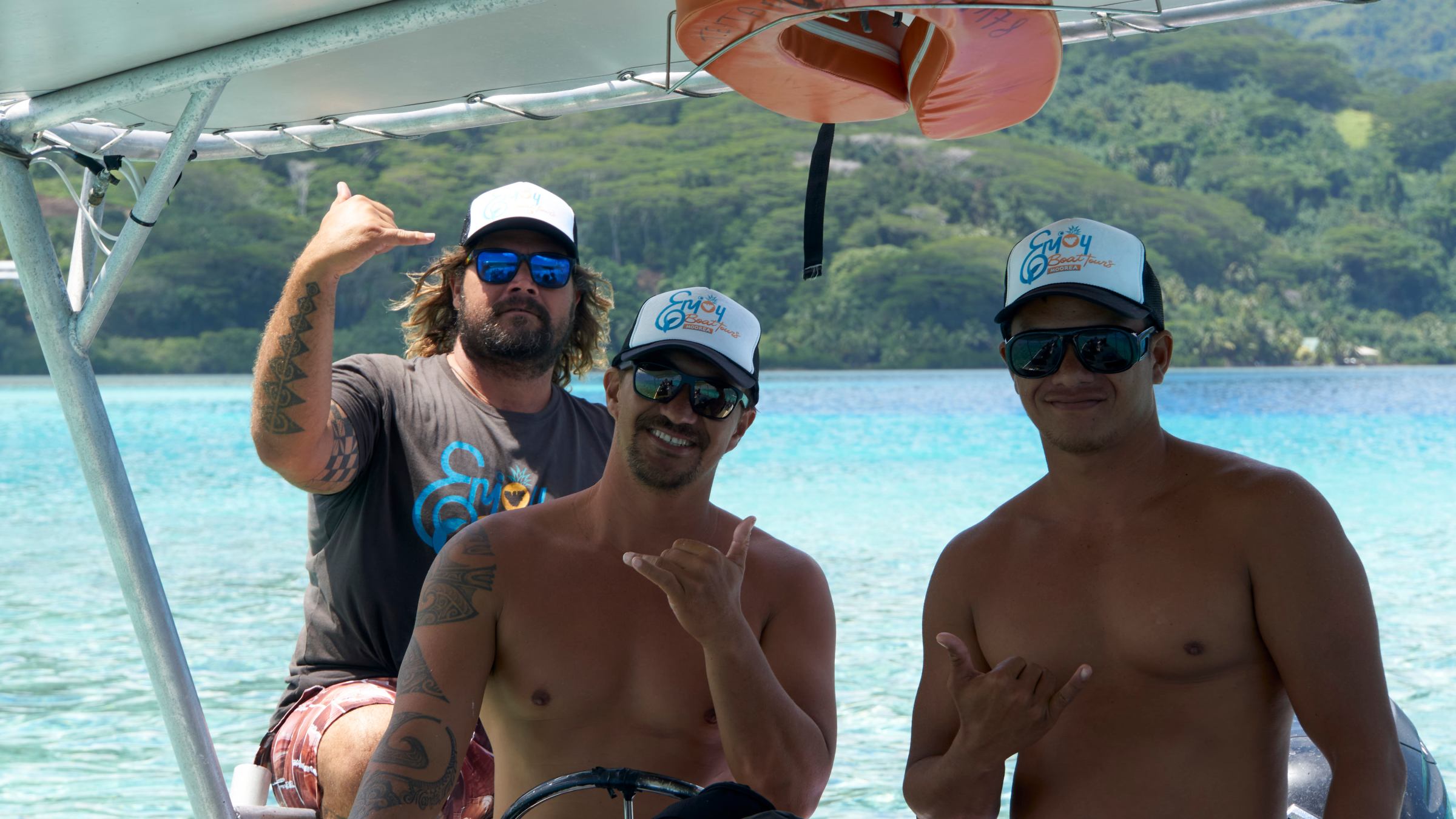 Three men on a boat, making shaka signs and wearing sunglasses and caps.