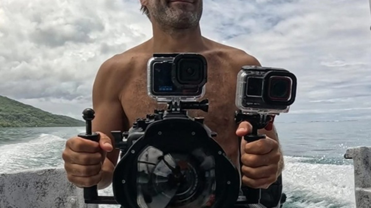 Man on a boat holding underwater camera equipment with two action cameras mounted.